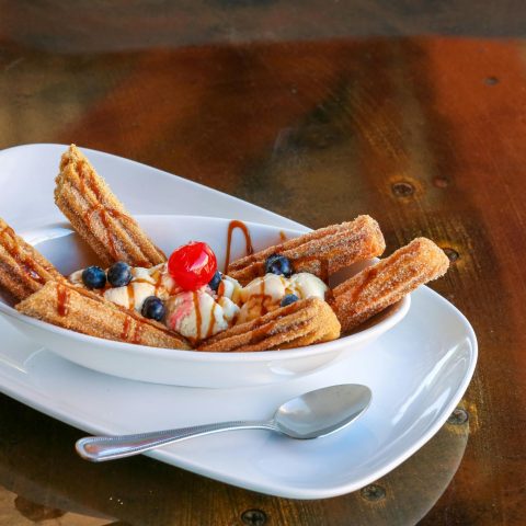 A tempting plate of churros served with ice cream, blueberries, and a cherry.